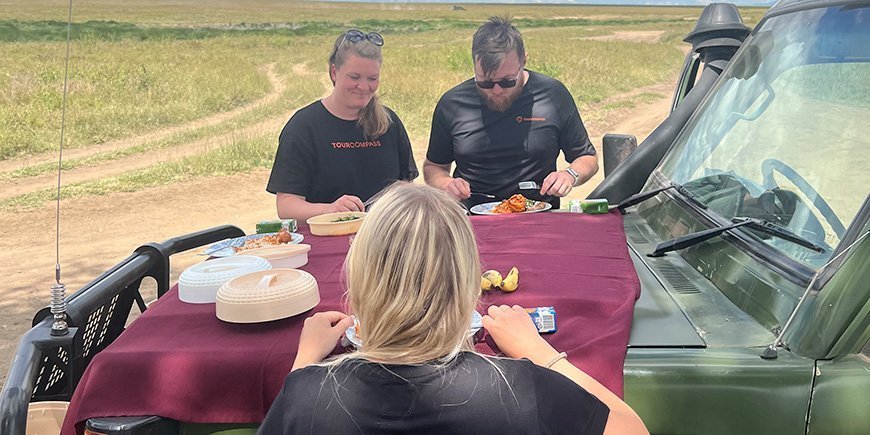 Three people eating breakfast by a jeep in Tanzania 