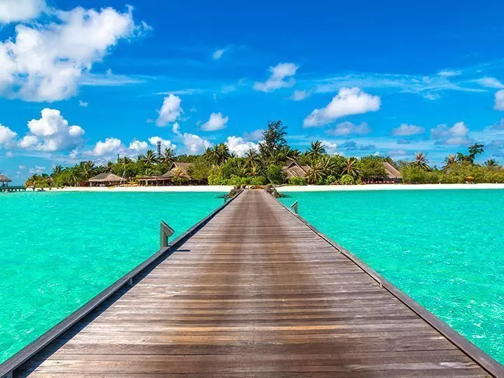 Water villas (bungalows) and wooden bridge on tropical beach in Maldives on a summer day