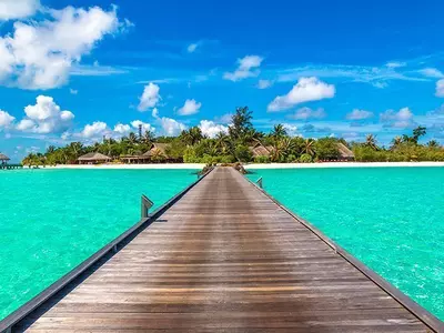 Water villas (bungalows) and wooden bridge on tropical beach in Maldives on a summer day