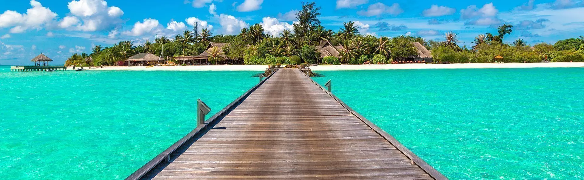 Water villas (bungalows) and wooden bridge on tropical beach in Maldives on a summer day